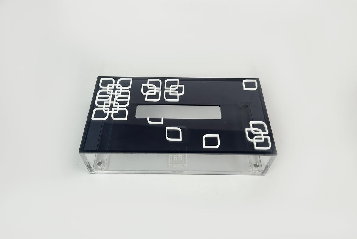 A clear acrylic tissue box with a black lid set with white square motifs; made to order by MASHQ