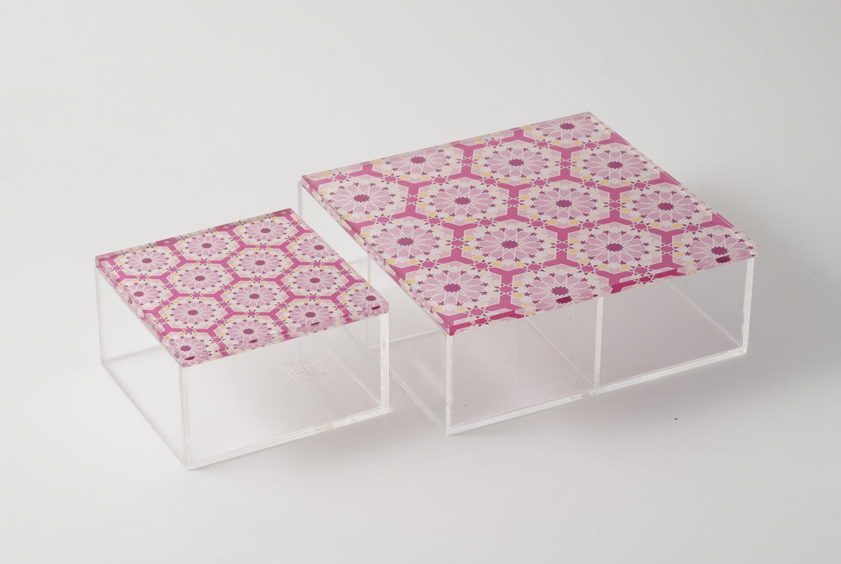Two pink arabesque lidded acrylic boxes seen from an angle