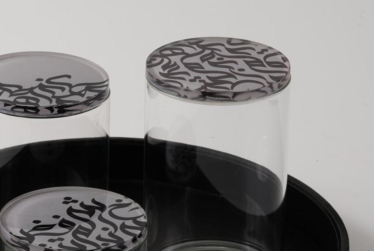 Glass jars with calligraphy lids standing on a black serving tray
