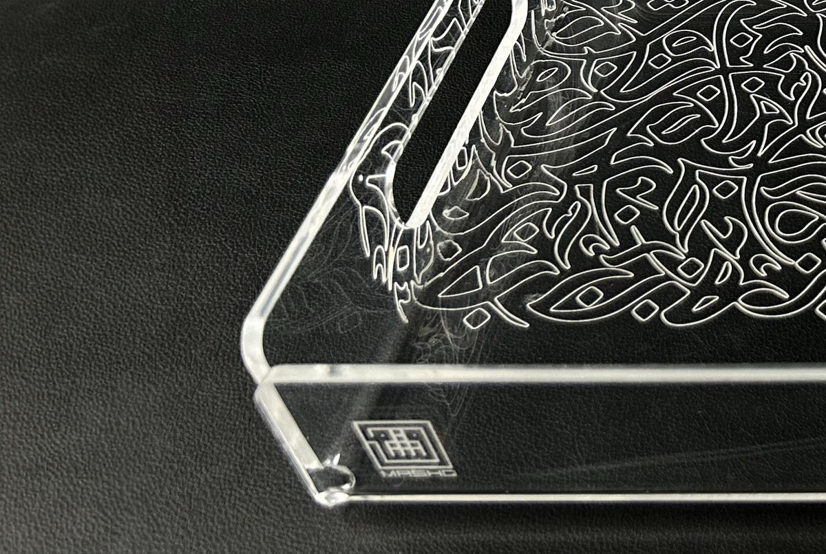 Clear acrylic tray with white arabesque engraving, on a dark leather surface