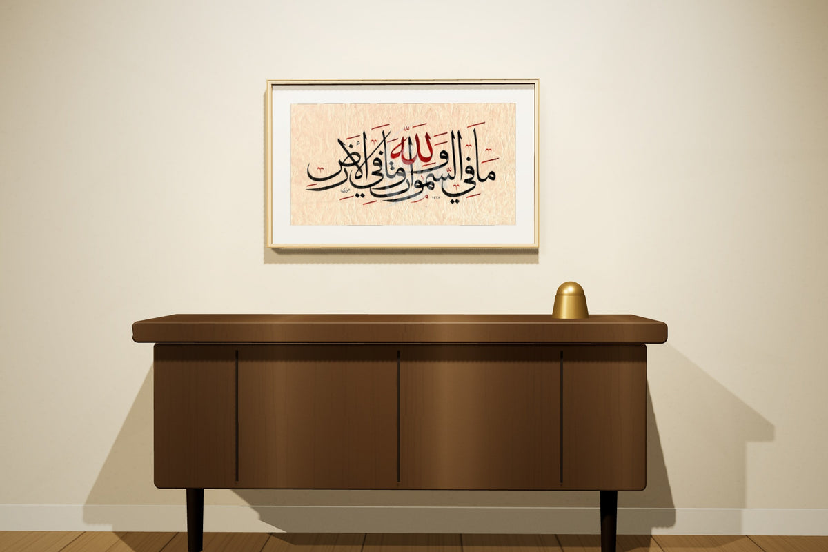 «لله ما في السموات وما في الأرض» بخط أحمد الهواري، 70 × 50 سم، معروضة بمقاسها الحقيقي في إطار سنديان طبيعي على جدار مجلس — التأطير متاح عند الطلب