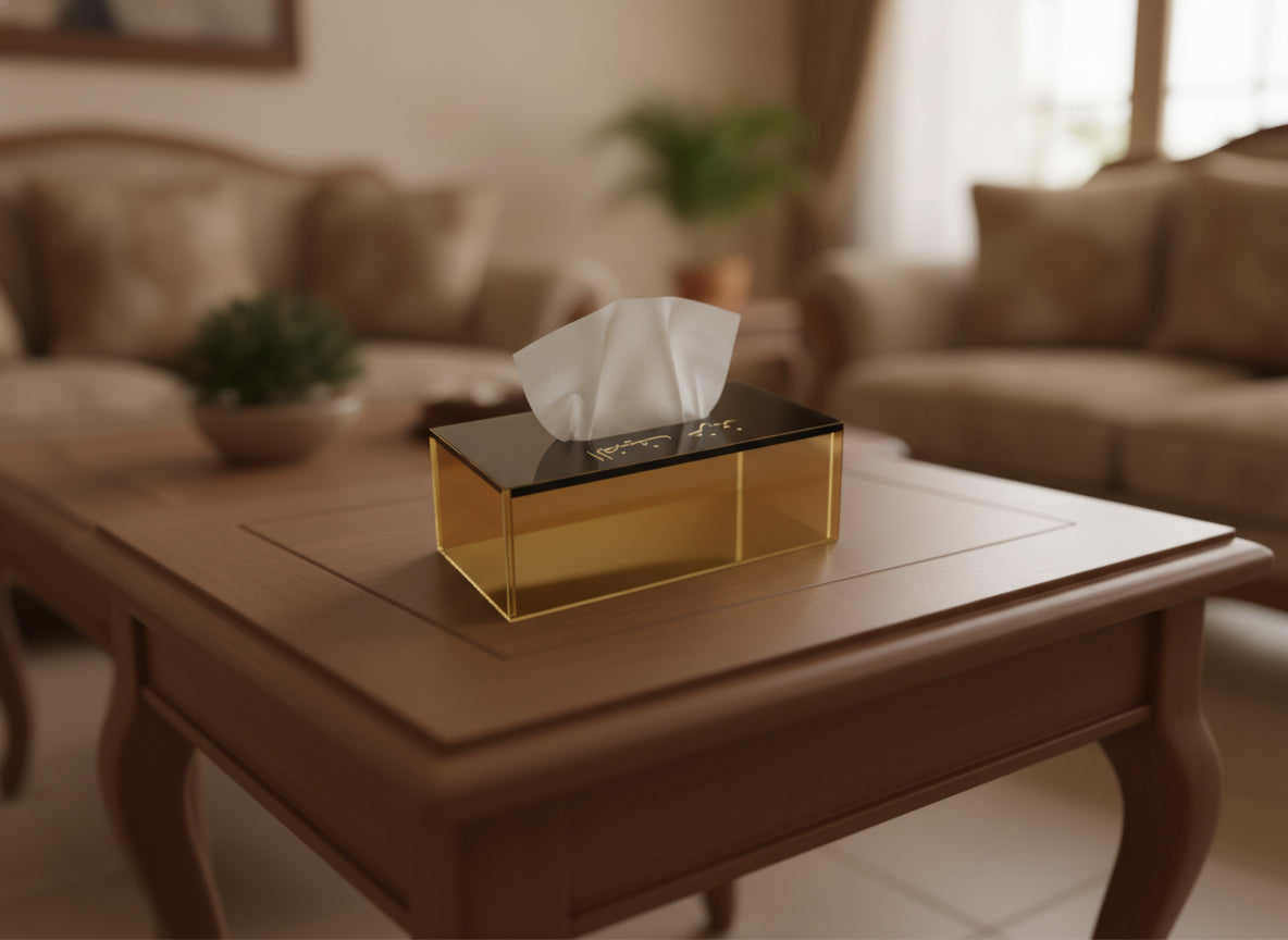 An amber acrylic tissue box with «الضيف عزيز» in Naskh on a living-room coffee table