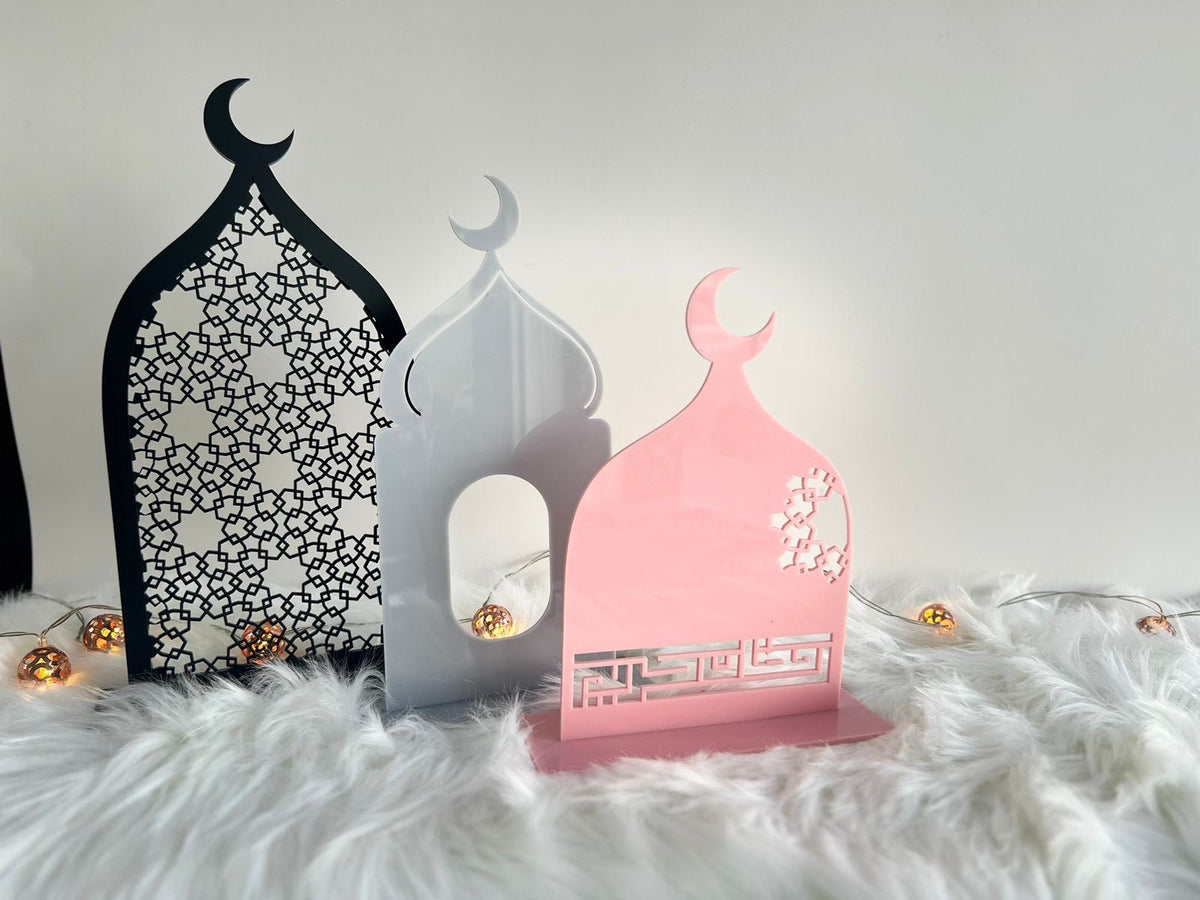 Three masjid-shaped acrylic Ramadan decorations in black arabesque, white and pink with Kufic calligraphy, lit by fairy lights