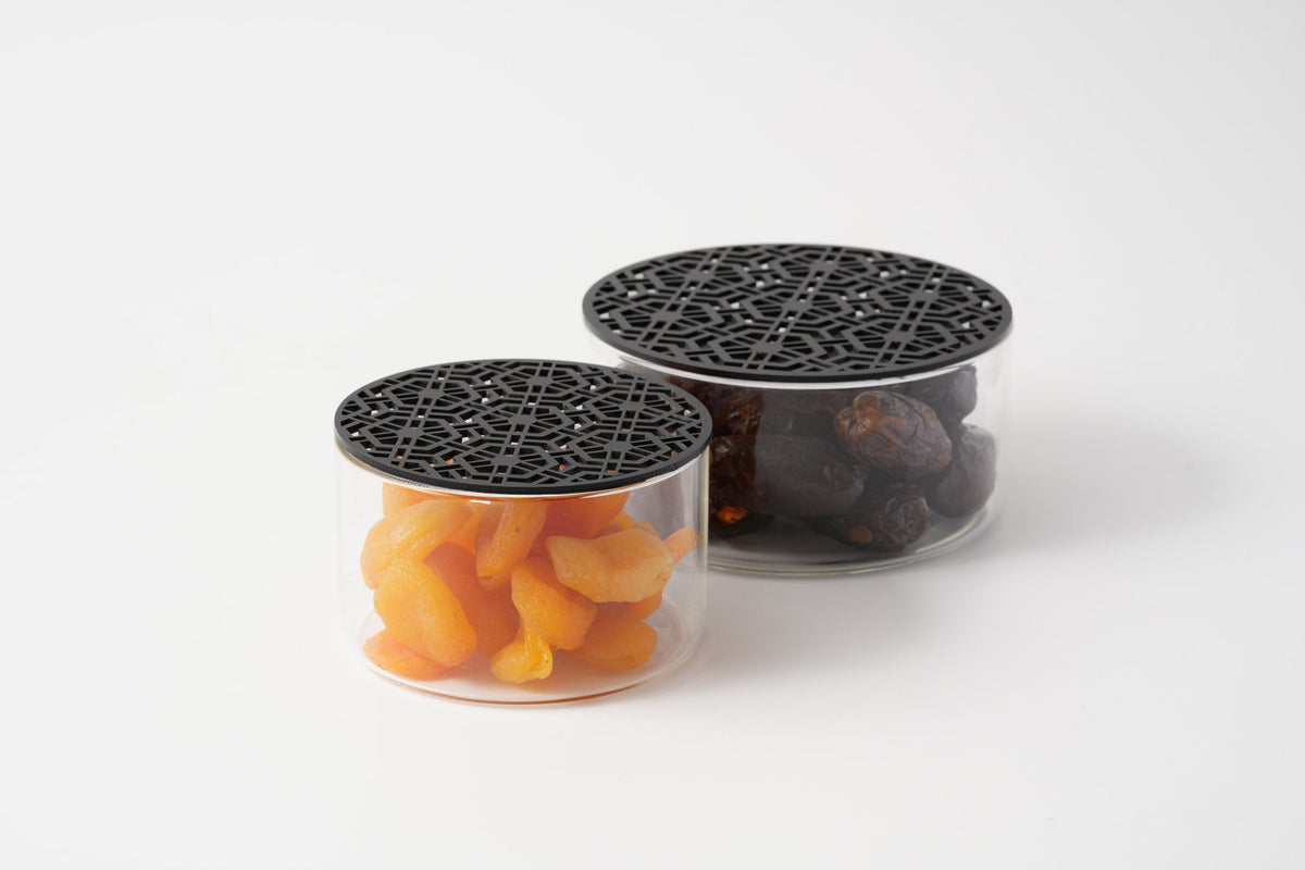Two glass jars of dried apricots and dates under black arabesque lids, made by MASHQ in the UAE