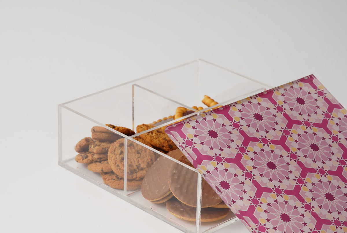 Clear acrylic box with a pink arabesque lid, open and filled with dates and biscuits