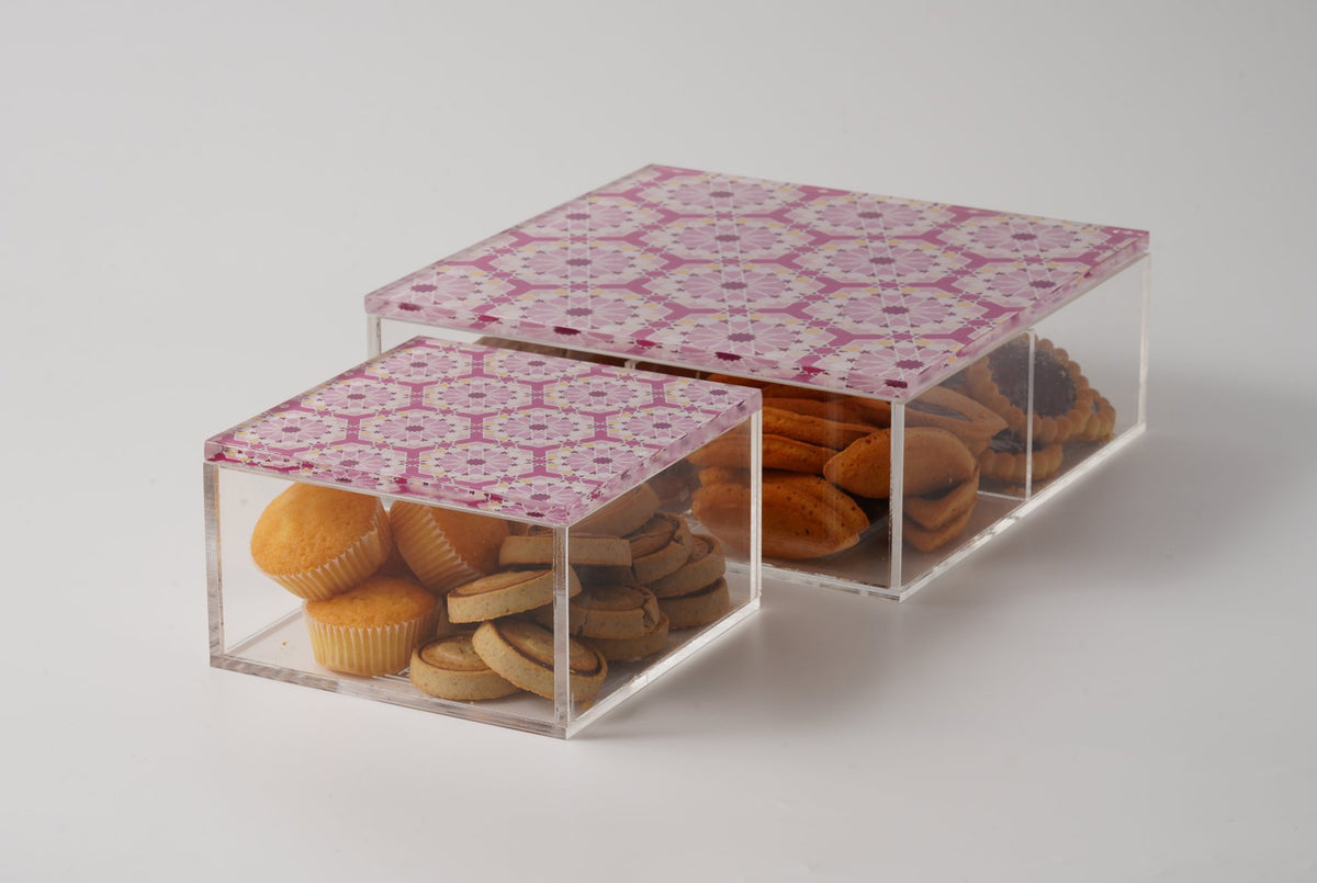Two clear acrylic boxes with pink arabesque lids, one holding biscuits